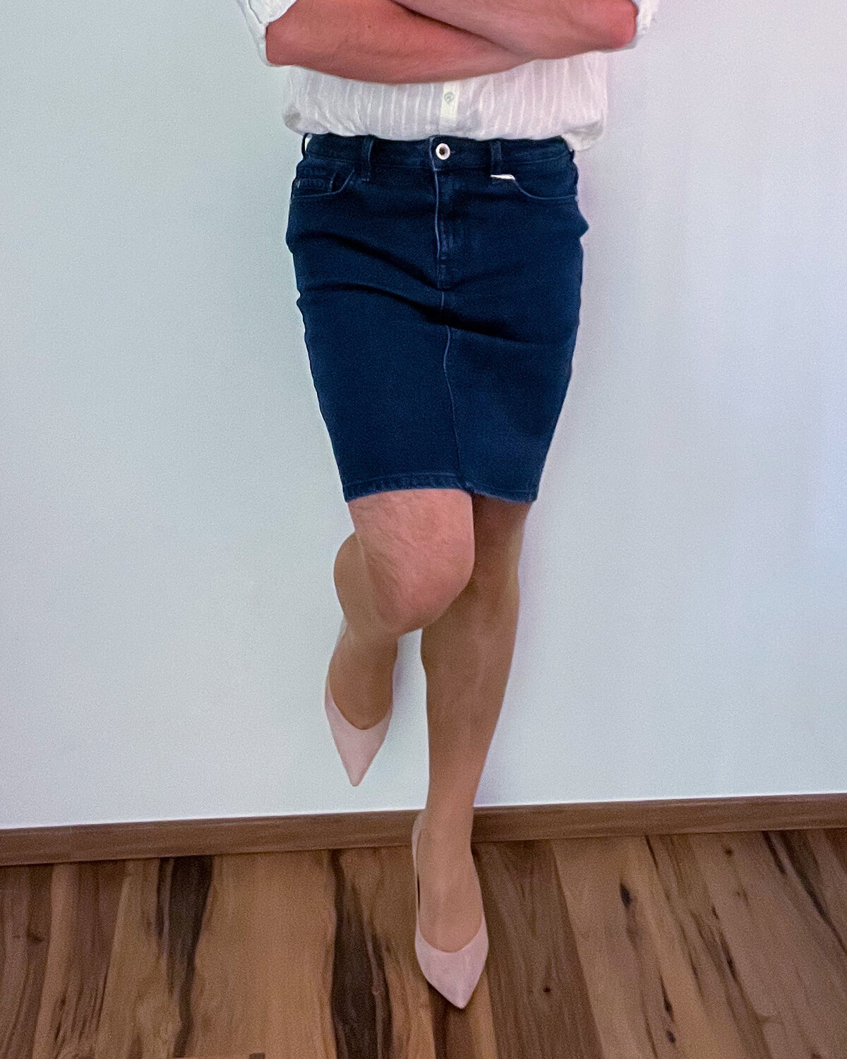 Übergeschlagenes Bein im Jeansrock mit nudefarbenem Pump und schlankem Absatz