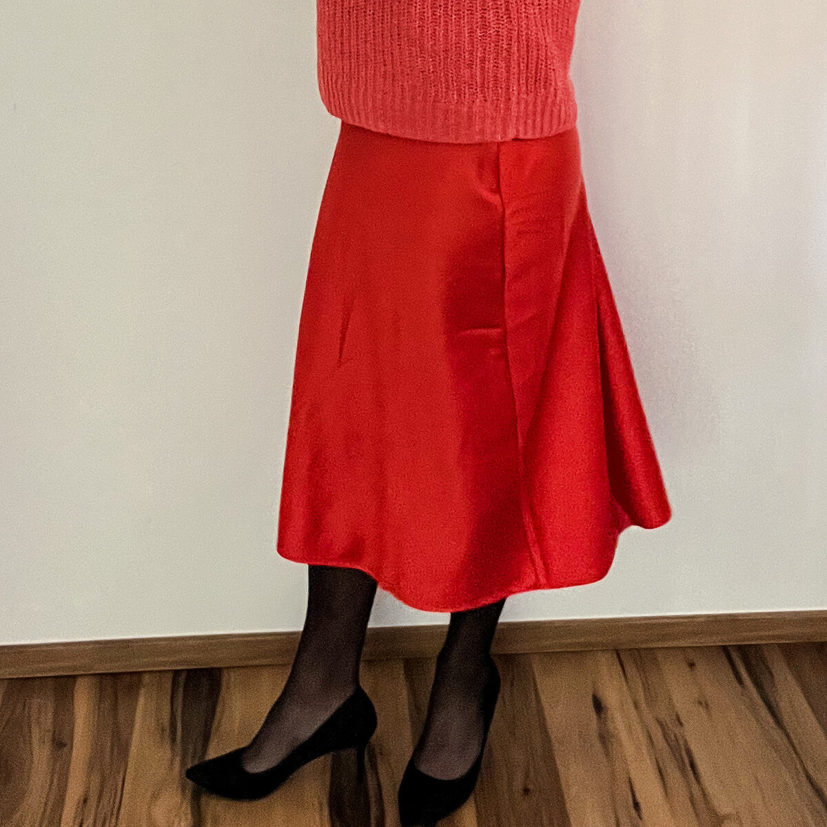 Seitenansicht: schwarze Pumps mit schlankem Absatz zu rotem Satinrock und schwarzer Strumpfhose