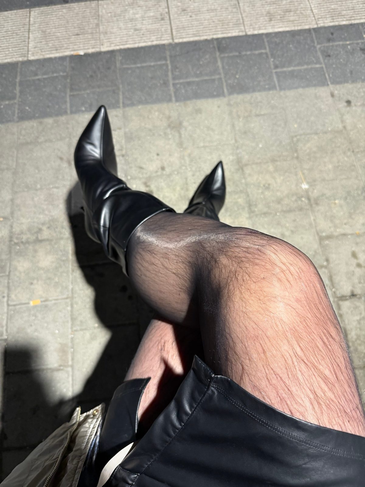 Schwarze Stiefel mit hohem Absatz, feine schwarze Strumpfhose und Lederrock auf Rillenplatten am Bahnsteig
